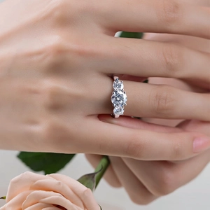 Three-stone S925 sterling silver moissanite engagement ring worn with a pink rose