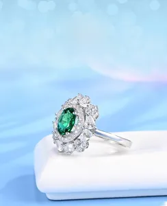 Macro view of floral halo ring with oval emerald and teardrop side stones on a white stand