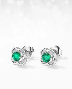 Macro detail of silver four-leaf clover stud earrings with emerald-green center stones