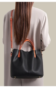 Detail of black pebbled leather tote bag featuring orange handles and gold metal studs