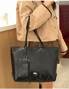 Detail of black leather tote bag with gold logo plaque and matching detachable pouch