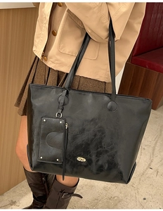 Detailed close-up of a black textured tote bag featuring a small decorative metal rivet pouch