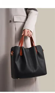 Detail of black pebbled leather tote with contrasting orange handles and gold hardware
