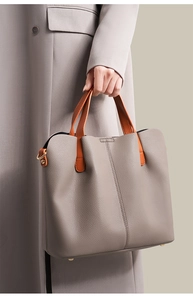 Detail of grey lychee leather tote with brown handles and gold hardware on purple coat