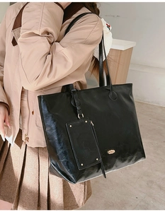 Close-up of black glossy leather tote bag with a small matching coin purse and shoulder strap