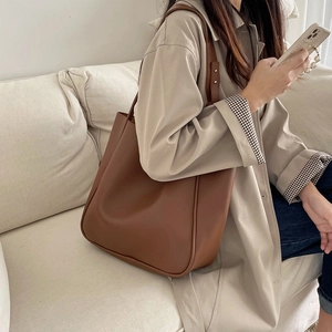 Large brown PU leather tote bag worn with a beige trench coat for a stylish office look