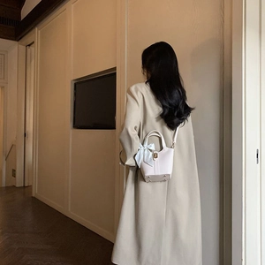 White bucket bag with blue silk ribbon detail shown on model in a long coat