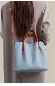Macro view of lychee grain leather texture and orange strap details on a grey tote bag