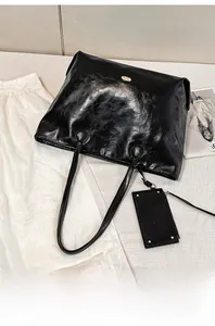 Detail of a black large tote bag in glossy leather finish with golden logo plaque