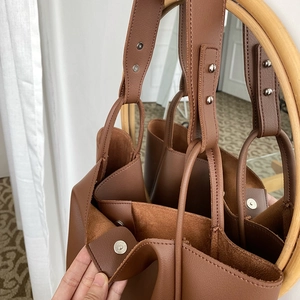 Close-up of brown leather tote bag showing magnetic buckle and wide shoulder strap