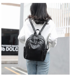 Close-up of a black leather backpack featuring multiple functional zipper pockets and side slots