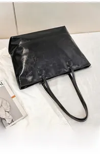 Close-up of black leather tote bag with glossy wrinkled texture and sleek shoulder strap