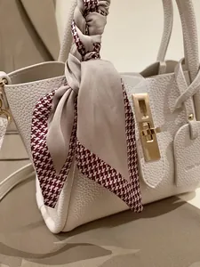 Gros plan du sac en cuir grainé beige avec foulard en soie pied-de-poule et fermoir doré