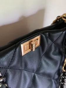 Detail of black quilted leather texture with gold metal turn-lock and chain strap