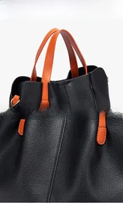 Detail of two-tone black pebble leather briefcase with orange handle and reinforced stitching