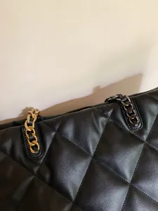 Close-up of black quilted leather tote bag with elegant gold and silver chain straps
