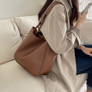 Detail view of a large vintage brown leather tote bag held by a model on a sofa