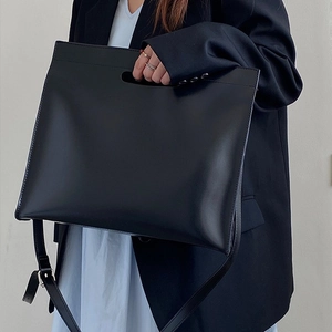 Minimalist black glossy leather tote bag with cutout handles and adjustable shoulder strap