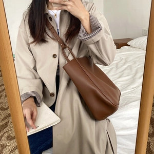 Detailed close-up of brown leather texture and adjustable metal buckle on tote bag