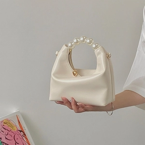 Detail of cream pearl handle handbag with a golden heart-shaped zipper charm and soft texture