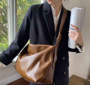 Detail of soft brown leather crossbody bag with wide strap and gold buckle
