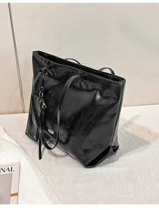 Detail of black glossy leather tote bag showing wax finish texture and metal logo