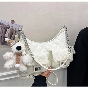 Détail d'un sac demi-lune blanc matelassé avec fermoirs argentés et breloque ours