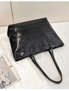 Detail of minimalist black leather tote bag showing glossy texture and refined stitching