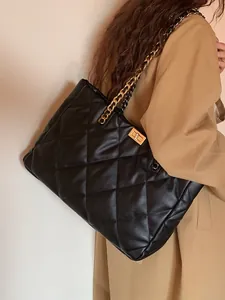 Detail of black quilted tote bag with gold chain strap worn with a beige trench coat