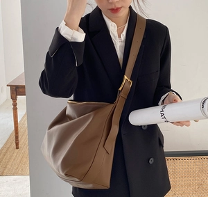 Detail view of large brown leather hobo bag with gold buckle on model with black suit