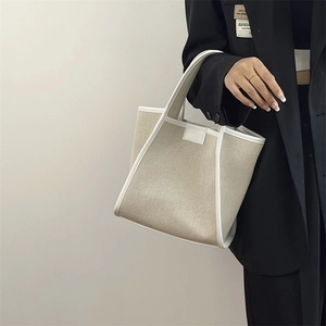 Chic beige canvas tote bag with white leather trim held by a model in a black blazer