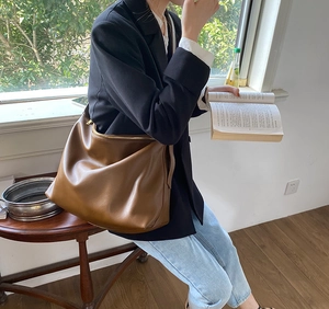 Brown leather large tote bag shown on a shoulder with a black blazer for office commute