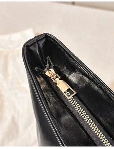 Close-up of golden metal zipper detail on black leather minimalist shoulder bag