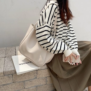 Side view of an oversized cream tote bag worn by a model against a minimalist wall
