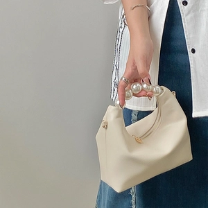 Detail of beige hobo bag with large pearl handle carried by a model in casual attire