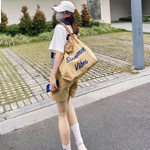 Outdoor shot of a khaki canvas tote bag with Summer Vibes embroidery and brown leather handles