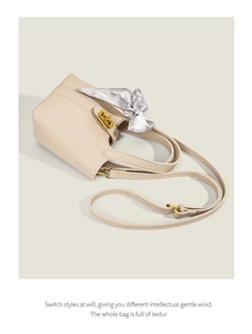 Close-up of beige lychee grain leather bucket bag with gold twist lock and silk scarf detail