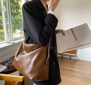 Detail of a large brown tote bag with matte synthetic leather texture and gold zipper