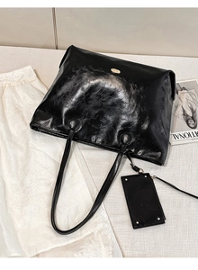 Detail of black glossy tote bag with gold logo plaque and matching pouch on white background