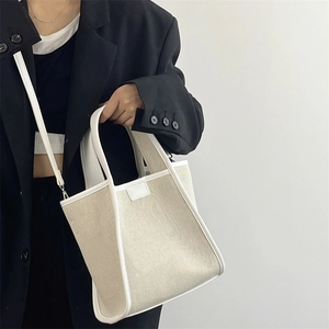 Minimalist beige canvas tote bag with white trim and detachable shoulder strap worn by model