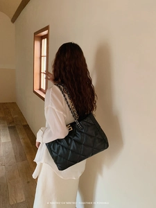 Close-up of black quilted chain tote bag worn by model in warm minimalist setting