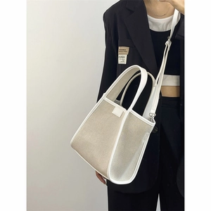 Detail of canvas tote bag showing top leather handles and adjustable shoulder strap