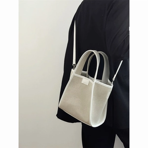 Canvas bucket tote bag with white leather trim shown in a minimalist side shoulder view