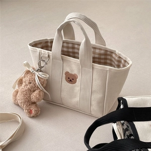 Detail of canvas tote bag with corduroy handles, bear embroidery and plush charm