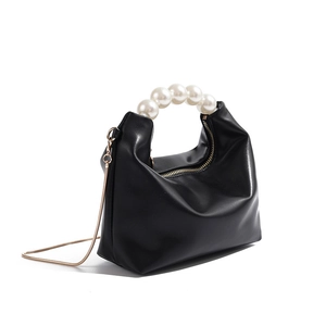 Detail of elegant black crescent bag featuring large pearl handle and gold snake chain