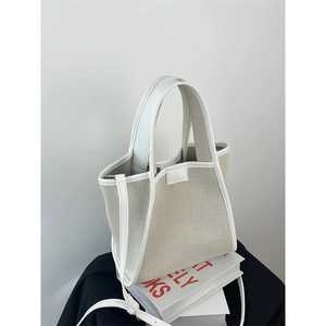 Detail shot of a beige canvas tote with white leather trim and adjustable shoulder strap