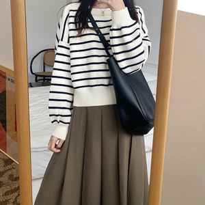 Minimalist black leather bucket bag worn with a striped sweater and brown pleated skirt