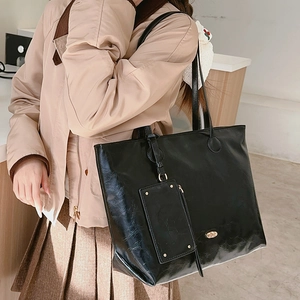 Minimalist black leather tote bag with glossy wrinkled texture and small detachable pouch