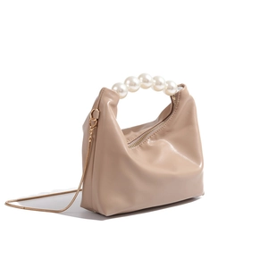 Detail view of mini beige dumpling bag with faux pearl handle and gold chain strap