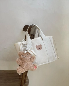 Detail of canvas tote with brown bear embroidery and plush charm hanging on a chair